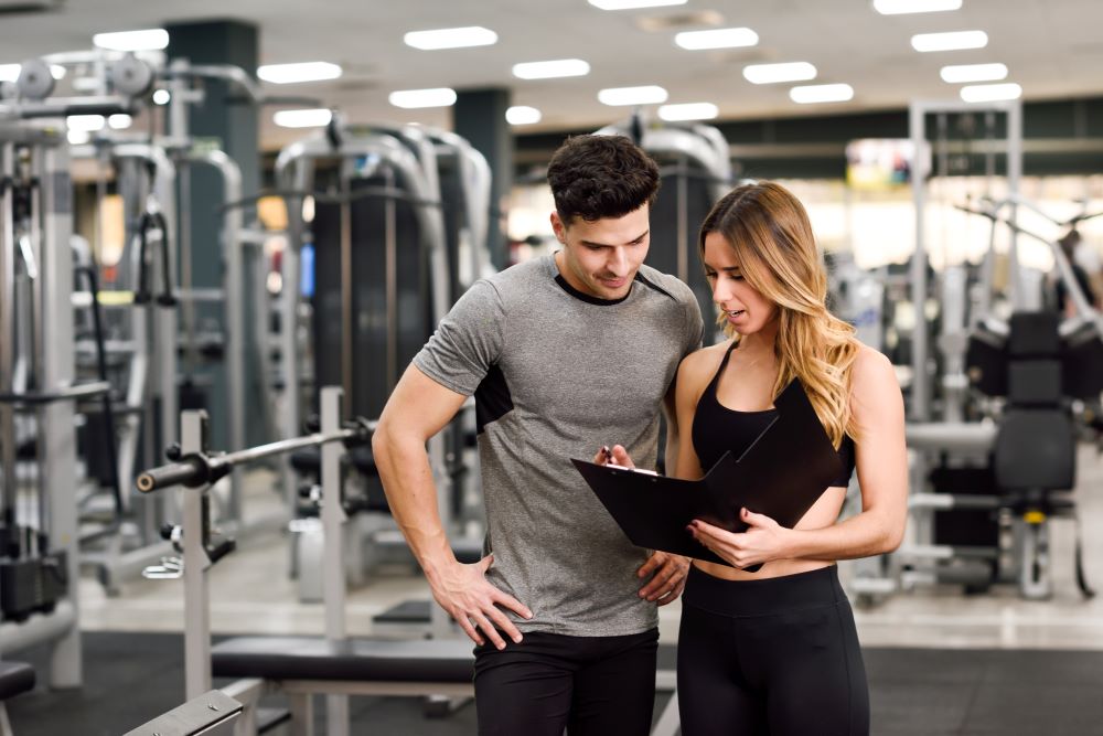 A man and woman in a gym looking at a clipboard.