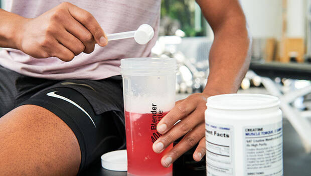 A man in a gym holding a bottle of supplements.