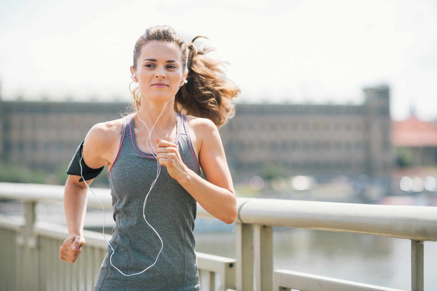A woman jogging on a bridge with earphones.