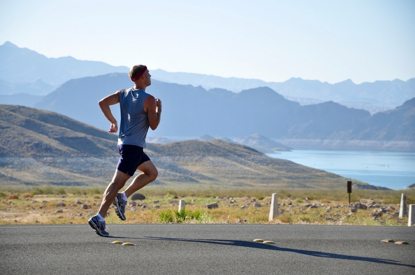 A man is jogging on a road with mountains in the background.