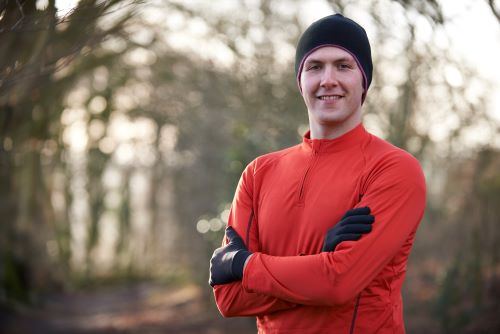 A man in a red shirt is standing in a wooded area.