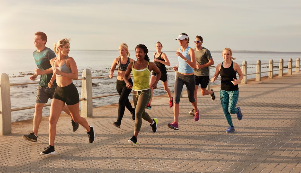A group of people jogging on a boardwalk near the ocean.
