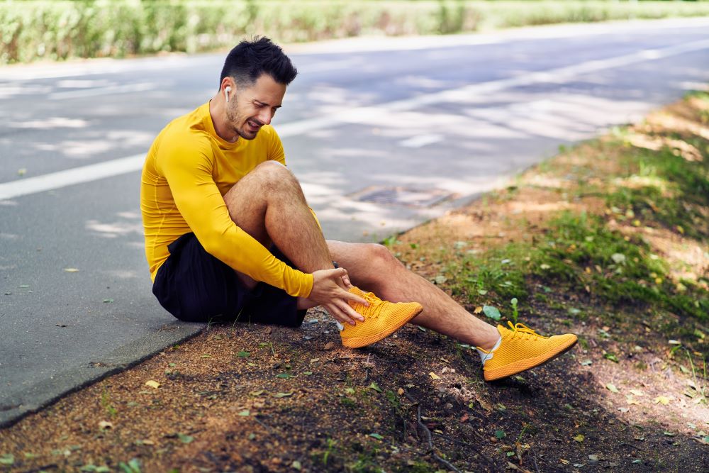 A man sitting on the side of the road with a swollen ankle.
