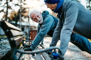 An older man and woman doing push ups on a park bench.