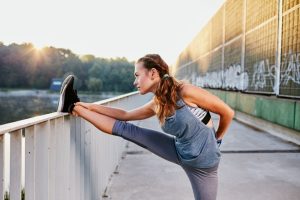 A young woman stretching her leg on a railing.