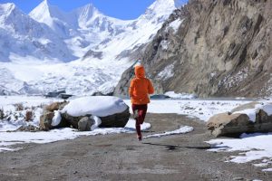 A person running on a snowy road in front of mountains.