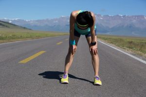 A woman is running on a road with mountains in the background.