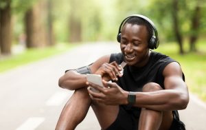 A man sitting on the road with headphones and a cell phone.