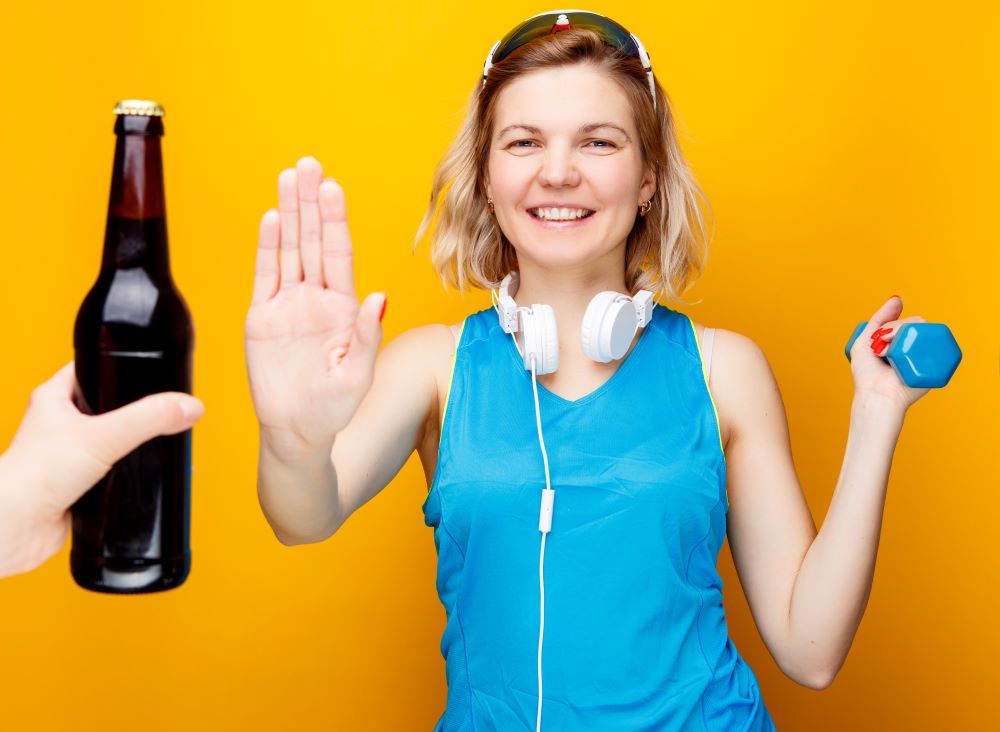 A woman holding a bottle of beer and a pair of dumbbells.