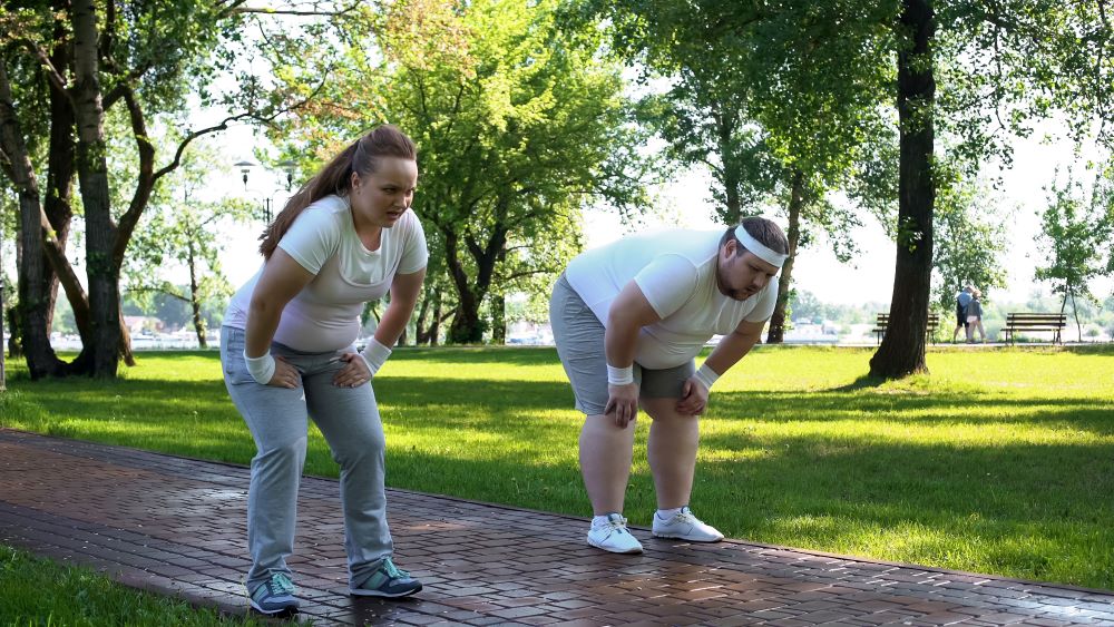 A man and a woman are doing squats in a park.