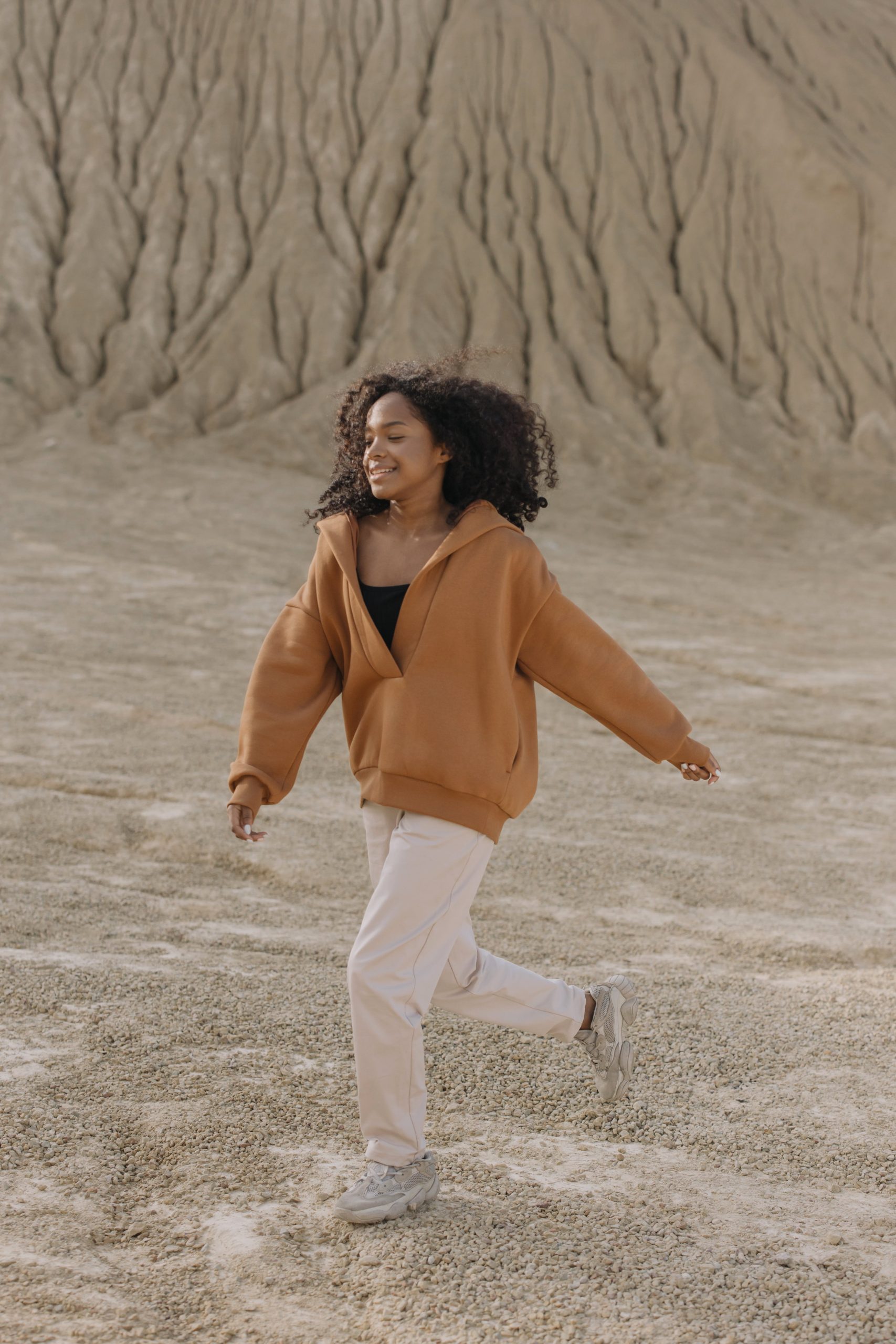 A woman in a tan sweatshirt running through a desert.