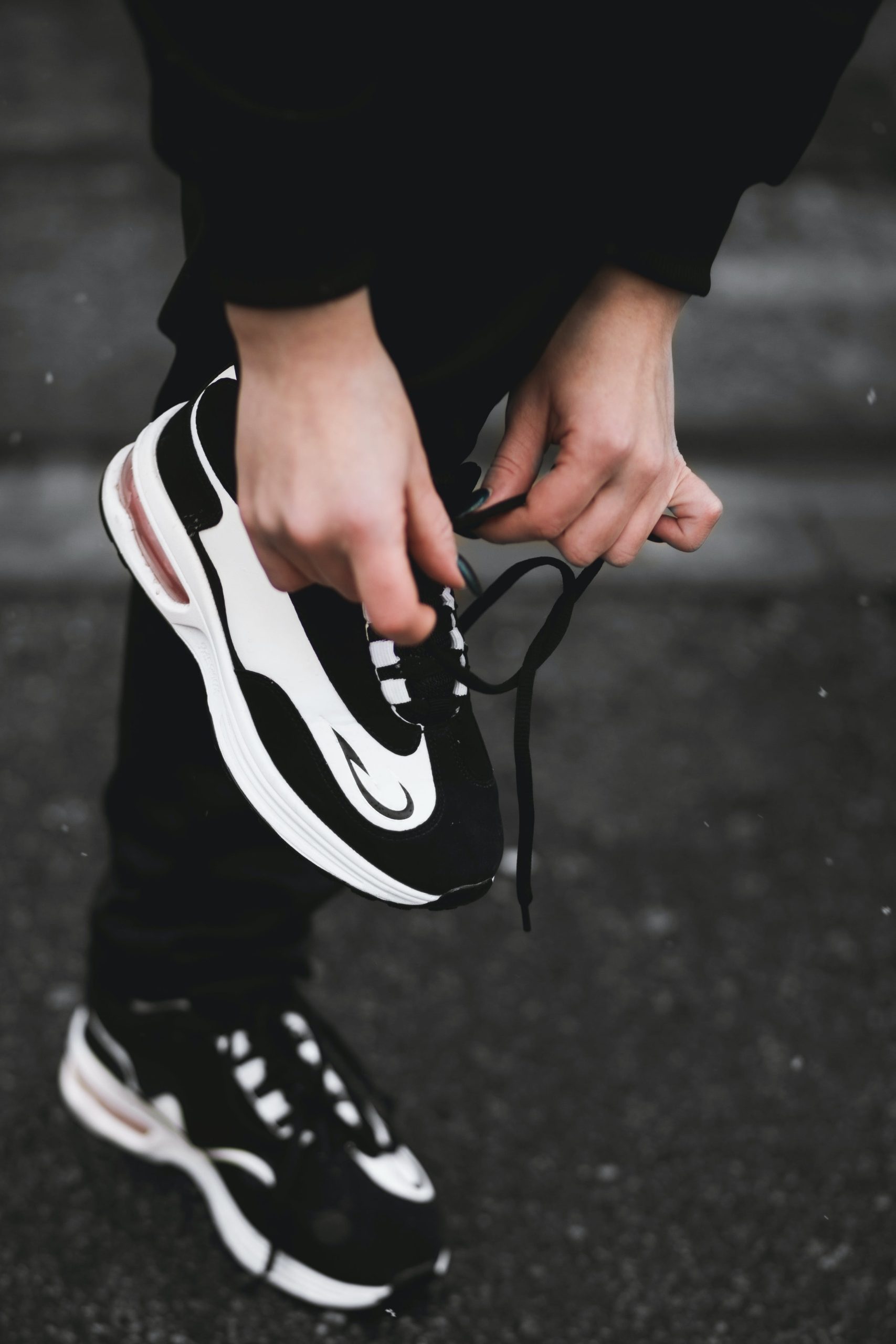 A person tying up a pair of black and white sneakers.