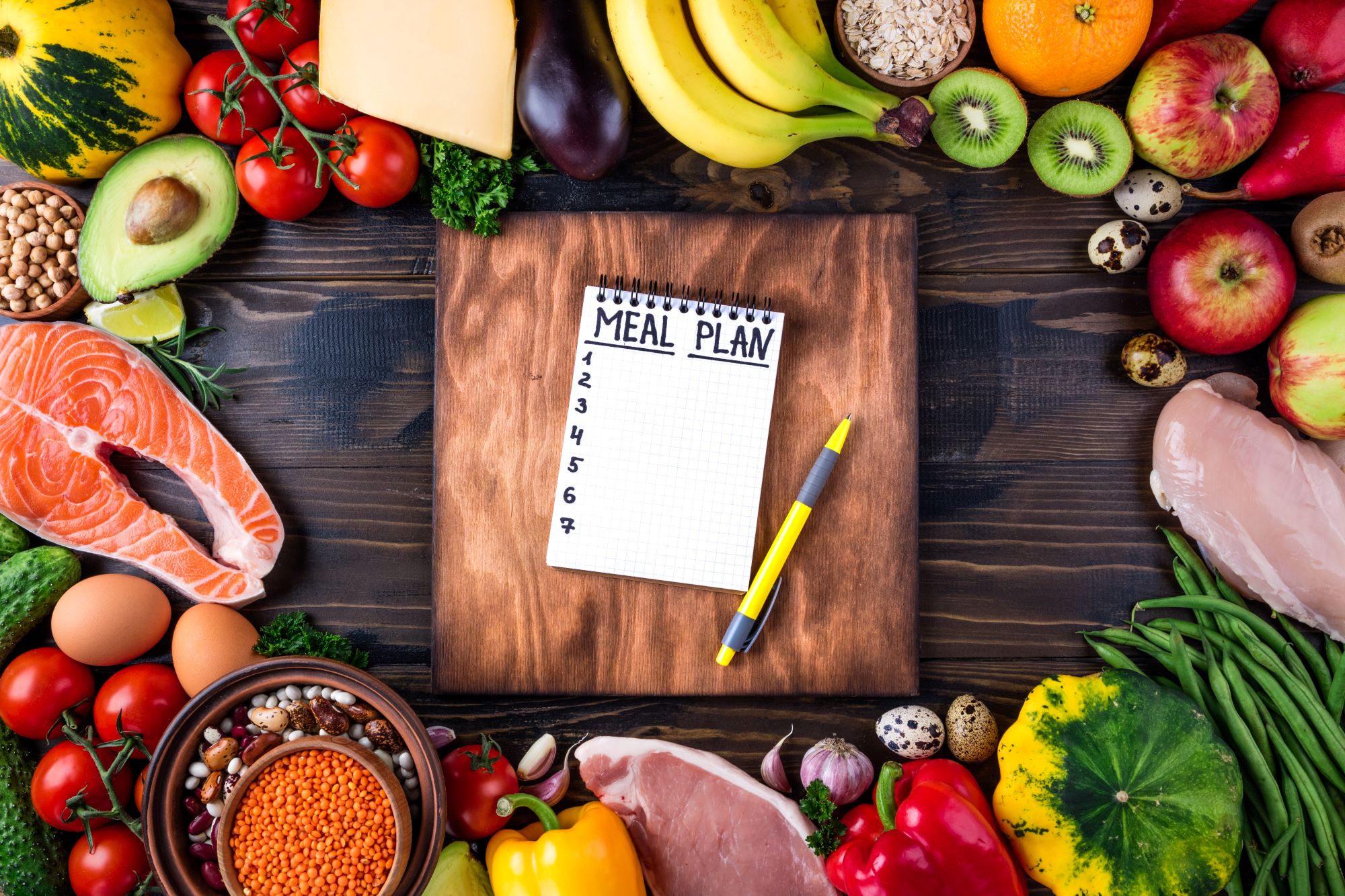 A notepad is surrounded by a variety of fruits and vegetables.