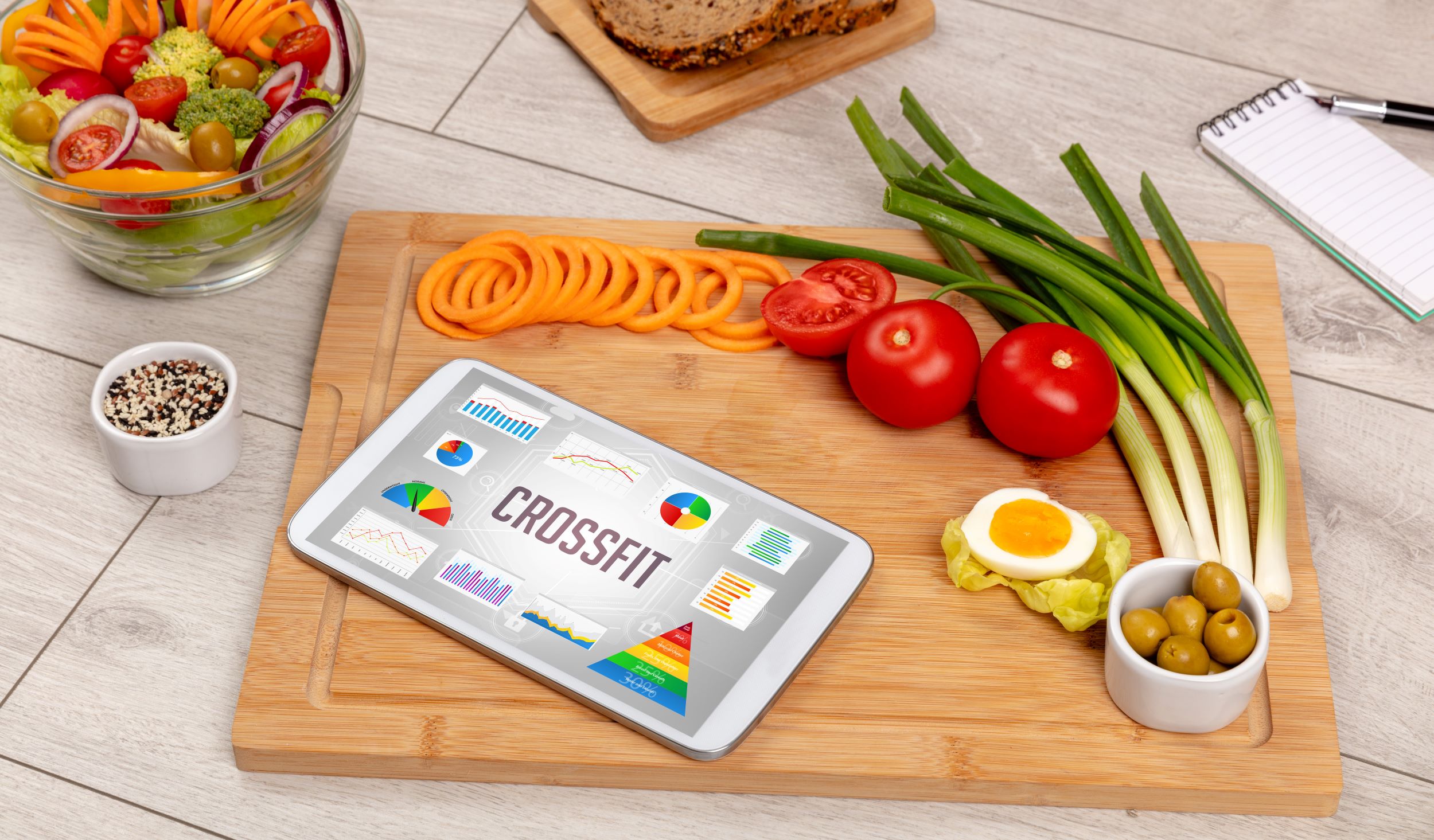 Healthy meal planning with a fitness app on a tablet amid fresh vegetables on a wooden table.