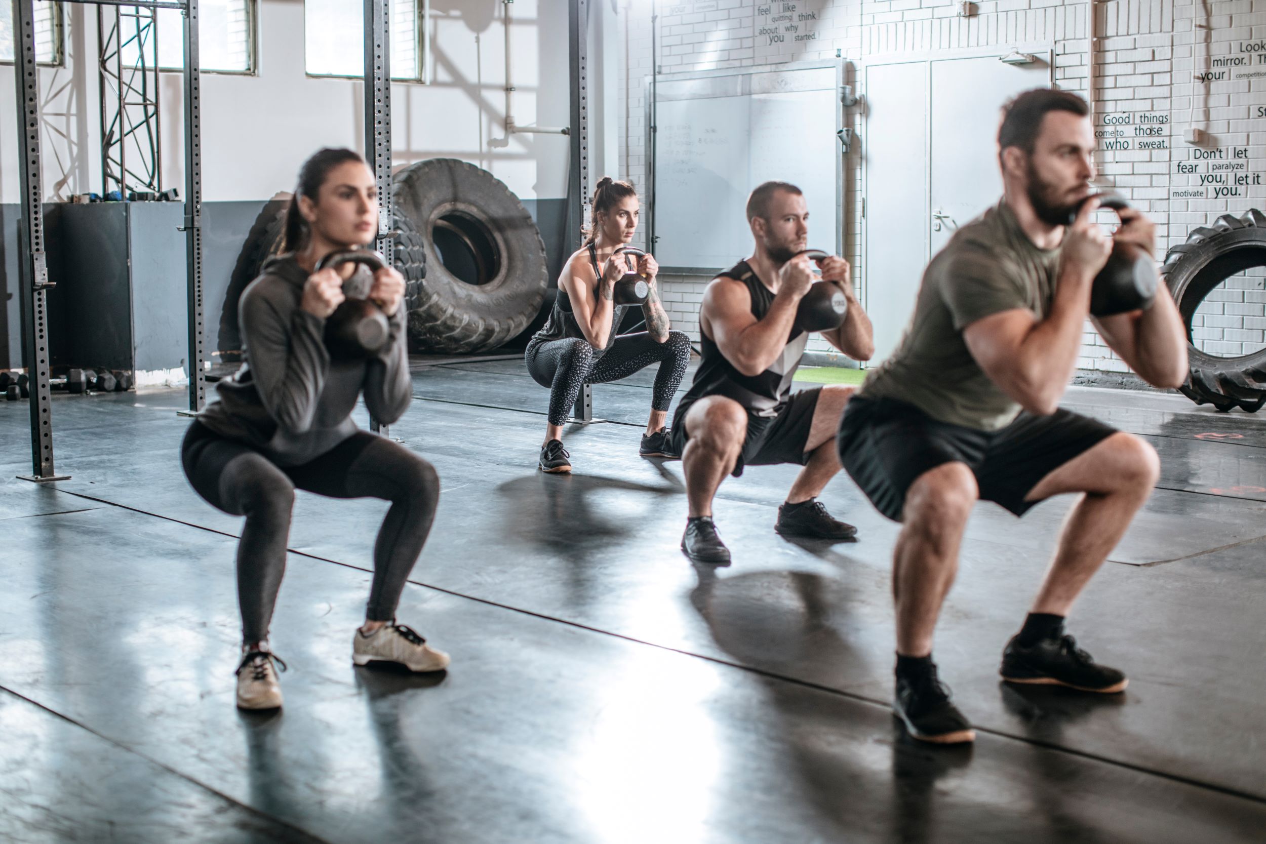 Three people performing squats with kettlebells in a gym.
