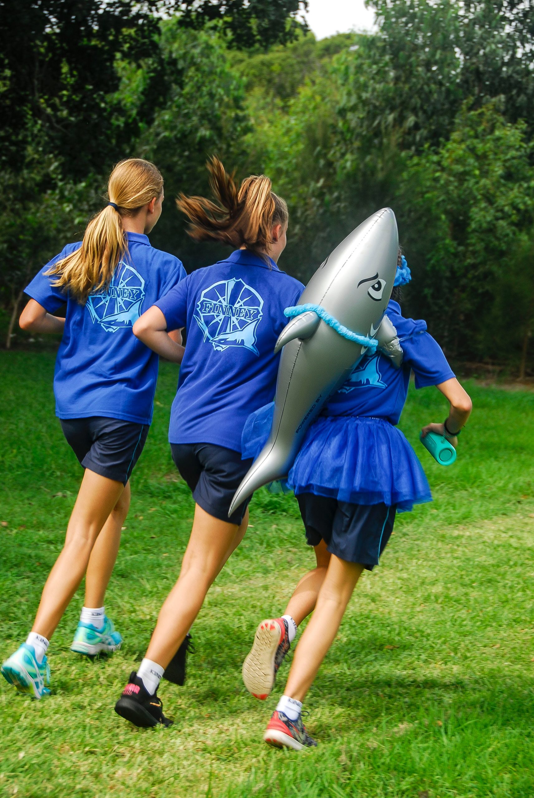 Three individuals participating in a running event, one of whom is holding an inflatable shark.