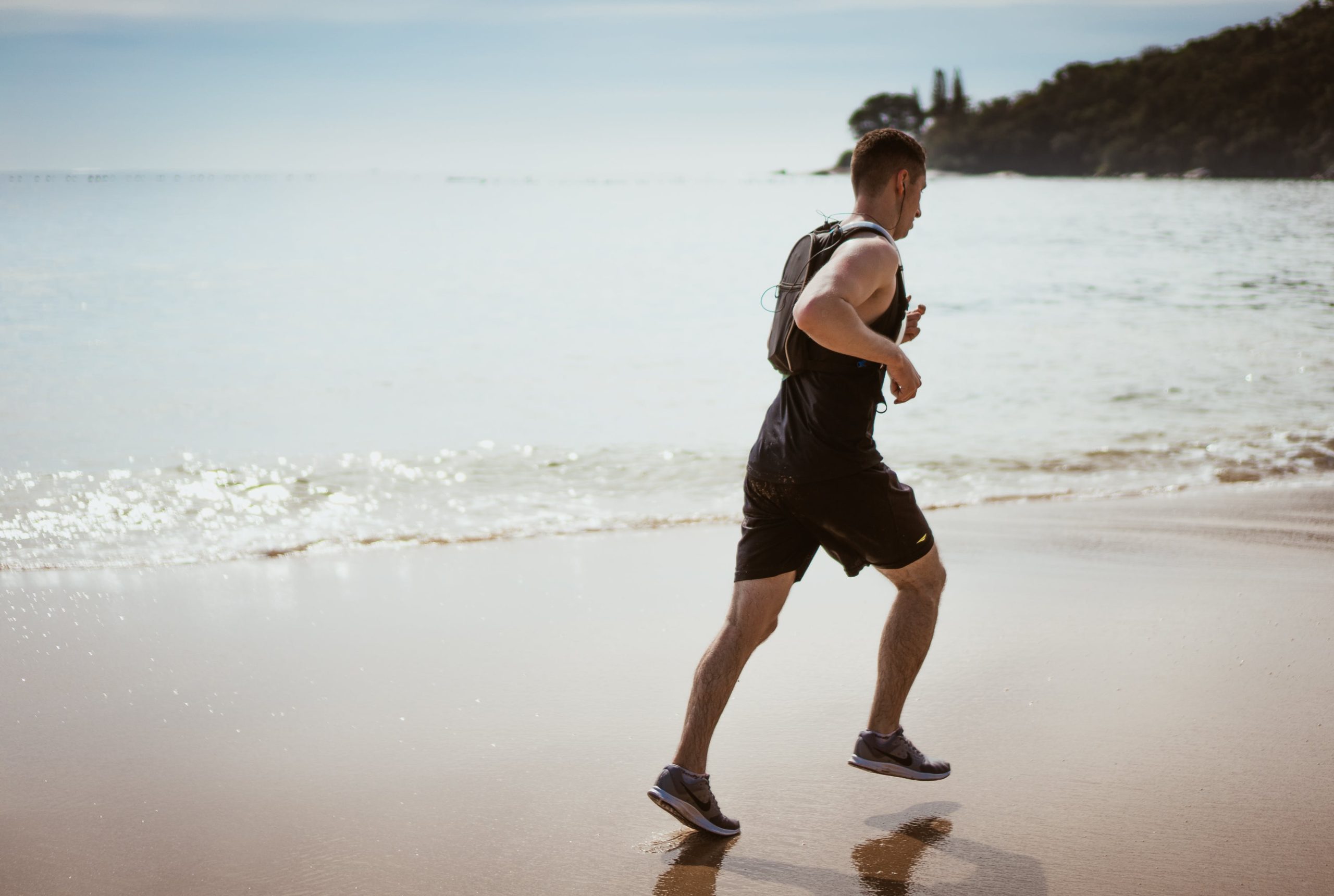 Man jogging along a beach shore at daytime.