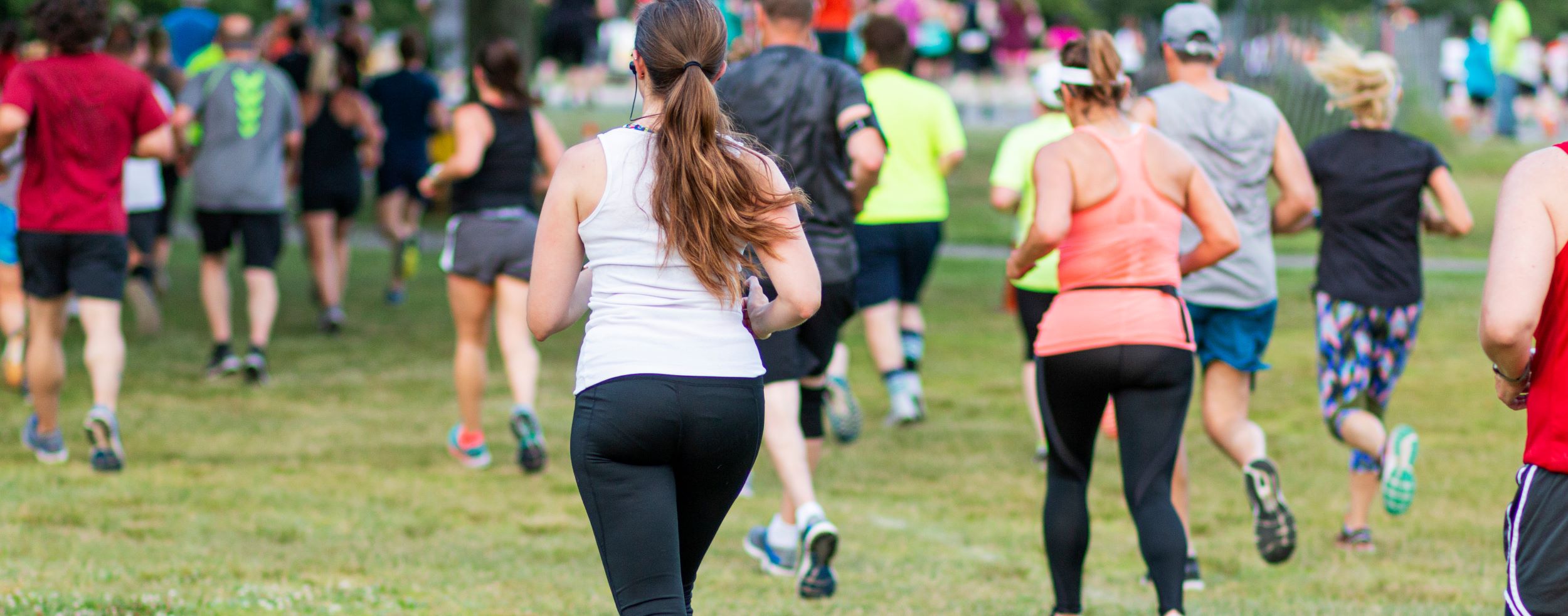 Group of people running in a park event, focused on a woman in a white shirt leading from the front.