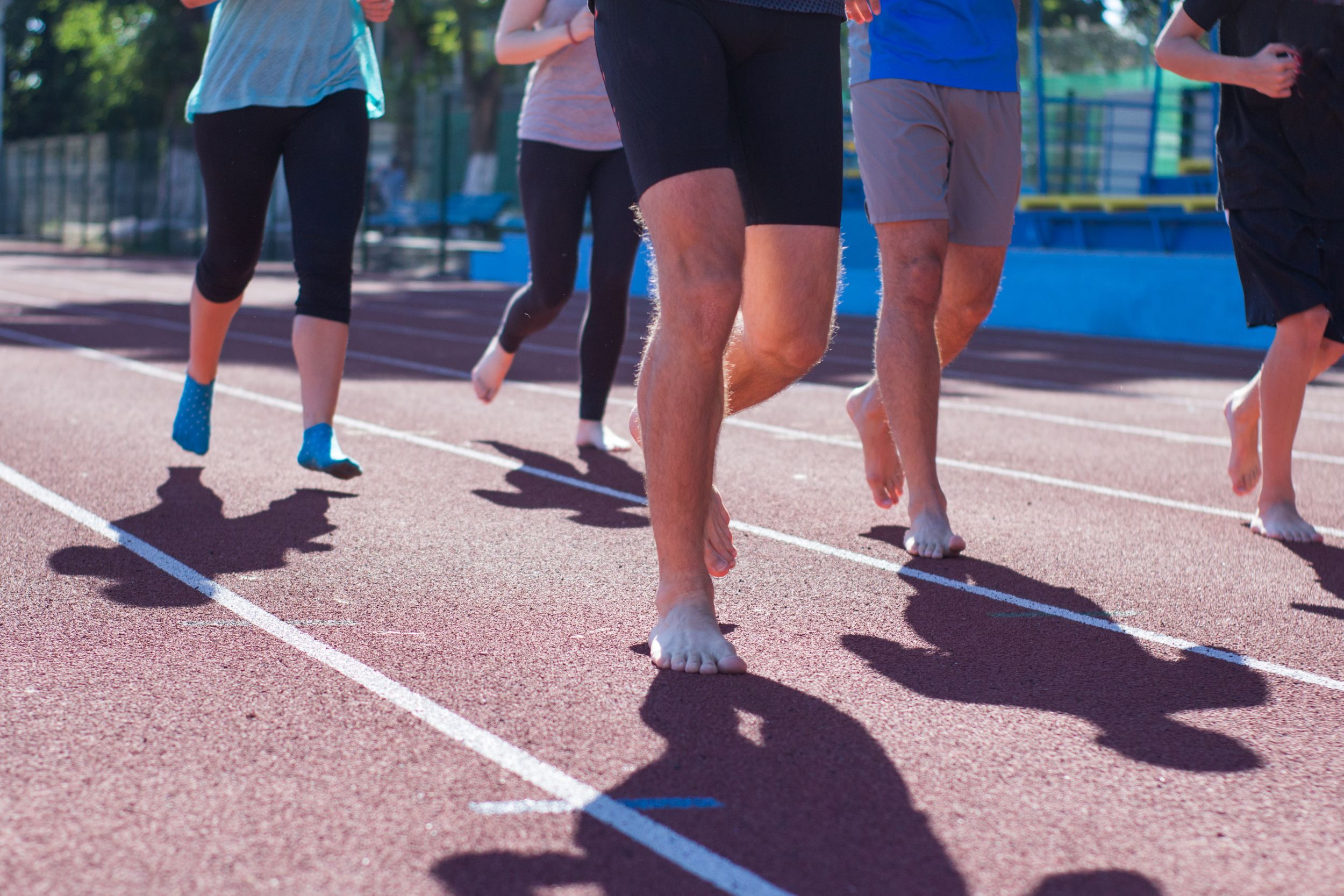 People running barefoot on a track during daytime.